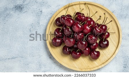 Delicious red ripe cherries in a wooden plate top view on gray background with copy space