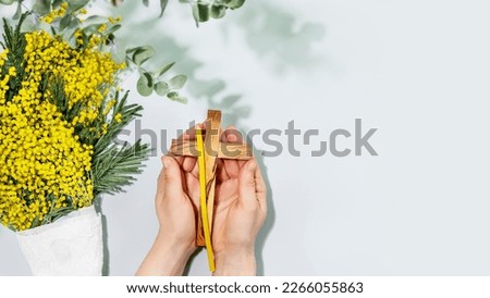 Easter religion banner. Womans hands hold wooden crucifixion and church candles on blue background with mimosa bouquet. Concept of Holy Week, Palm Sunday, Lent and religion holidays. Copy space