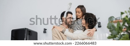 Smiling woman and daughter hugging man with Easter headband in kitchen, banner