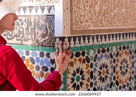 Woman in red  dress touching  ceramic wall with floral pattern by hand in henna painting in marrakesc, marocco