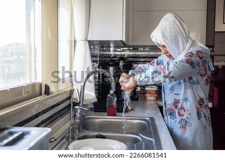 Middle-aged muslim woman does housework Kitchen cleaning sink wearing hijab headscarf. Islamic female washing home dishes. Housewife daily household life routine. Royalty-Free Stock Photo #2266081541