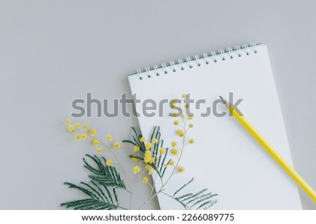 Notebook with blank page, mimosa flower and pencil on light grey background. Flat lay. Place for text.