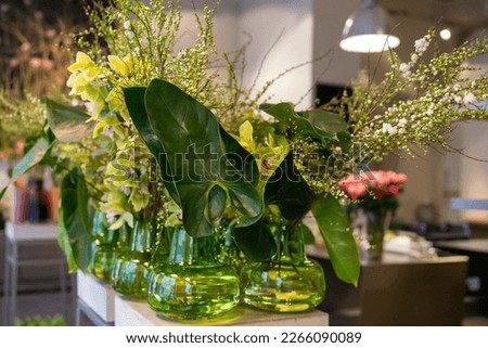 Decorative glass vases with flowers. Green Philodendron Burle-marxii and Gloriosa superba in the foreground.