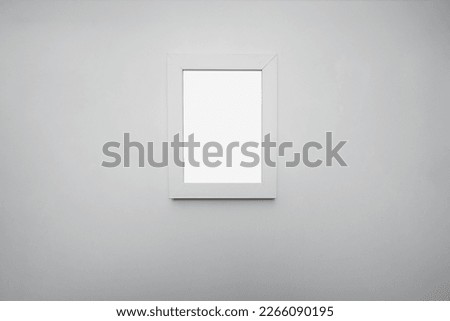 Empty white wooden photo frame with mockup space hanging on wall at home or office room. Portrait orientation picture with wood border.