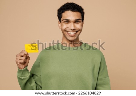 Young happy man of African American ethnicity wear green sweatshirt hold in hand mock up of credit bank card isolated on plain pastel light beige background studio portrait. People lifestyle concept Royalty-Free Stock Photo #2266104829