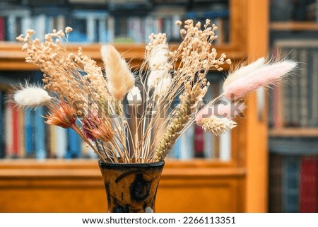 side view of bouquet of dried plants in vase close up with blurred bookrack on background