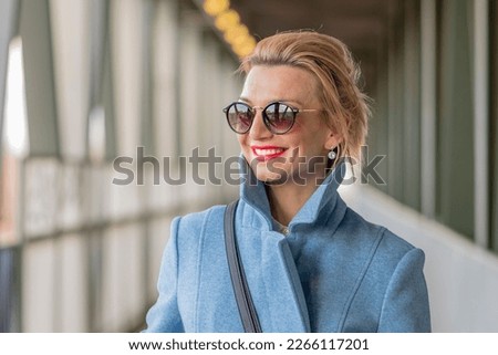Street portrait of a happy blonde woman 40-45 years old with glasses on a blurred urban background.