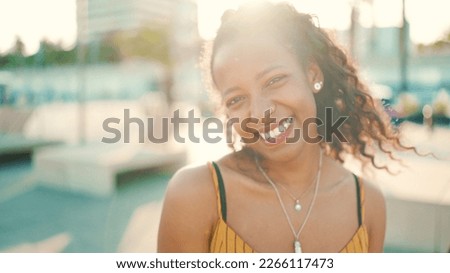 Closeup portrait of smiling woman with long curly hair on urban city background. Frontal close-up of happy girl fixing her hair and looking at the camera