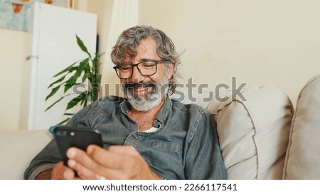 Middle-aged man relaxing on his couch while in home and using his smartphone to text Royalty-Free Stock Photo #2266117541