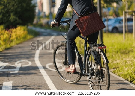 Anonymous male manager in business outfit riding on bike lane in sunny morning. Crop view of executive with leather briefcase getting to work by bike on bikeway outdoor. Concept of eco transport.