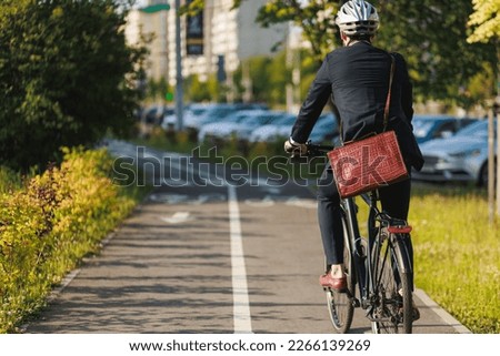 Elegant entrepreneur in smart casual cycling on bicycle track in warm sunny day. Back view of tall male manager with brown leather laptop bag riding bike in sleeping area of city. Concept of activity. Royalty-Free Stock Photo #2266139269
