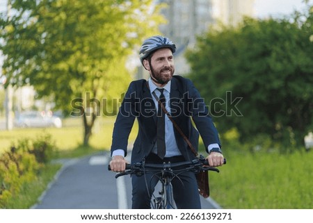Young male manager in business suit commuting to work on bike lane in early morning. Portrait of happy bearded executive driving bicycle, while looking ahead at sunny day. Concept of eco transport. 