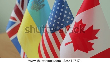 Small flags of different countries on table. Flags of Canada, American, United Kingdom, Ukraineon the desk in focus.