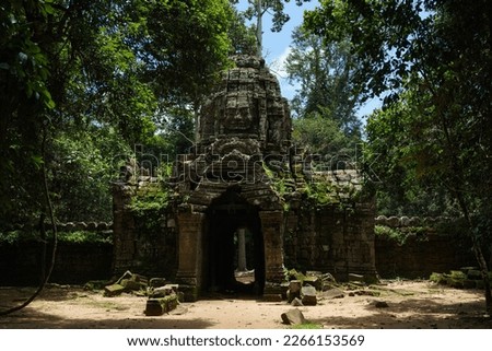 A photo of one of the gopuras at the Ta Som Temple site. It is constructed in the Bayon Style with a large carved stone face looking out from the top. Moss and foliage grow from the weathered stone. Royalty-Free Stock Photo #2266153569