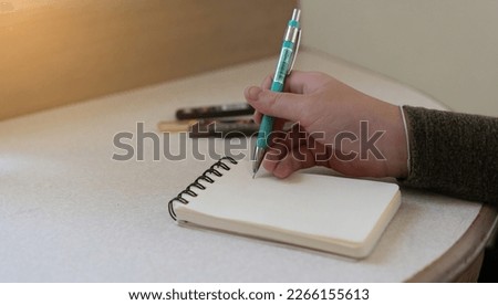 child hand use mechanical pencil writing on paper notebook