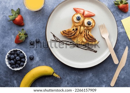 Homemade keto diet pancakes in the shape of an owl, served with fruit and juice.