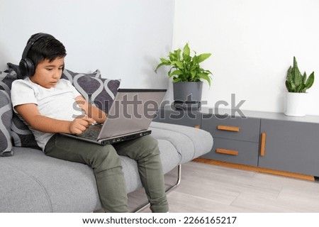 9-year-old Hispanic boy plays video games on his laptop with headphones leading to being overweight and poor sitting posture Royalty-Free Stock Photo #2266165217