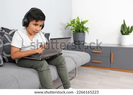 9-year-old Hispanic boy plays video games on his laptop with headphones leading to being overweight and poor sitting posture Royalty-Free Stock Photo #2266165223