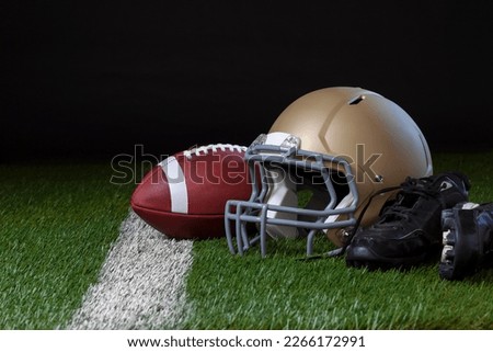 Football helmet with football and cleats on a grass field with a white stripe and dark background