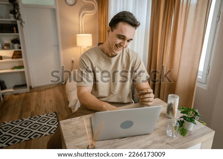 One man adult caucasian male sit at home happy smile at laptop computer hold bank credit card online shopping concept real people copy space e-commerce