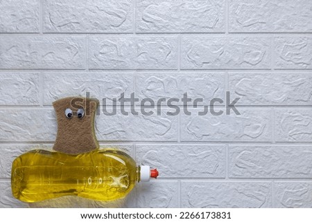 Funny composition and homework clean up. Top view. Copy space. Fun cleaning.Kitchen sponge with eyes sits on detergent on white brick wall background. Flat lay. Template for advertisement, billboard. 