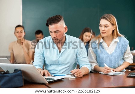 Adult students are retrained in the classroom of the university. Woman helping man to solve problem on laptop Royalty-Free Stock Photo #2266182129