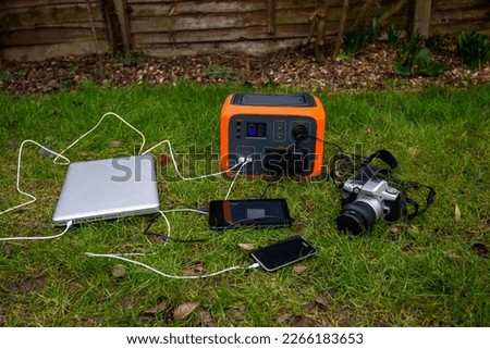 Portable power station solar electricity generator with laptop, tablet and camera electronic devices charging outdoors on garden lawn grass. Wireless charging lithium battery backup for use anywhere. Royalty-Free Stock Photo #2266183653