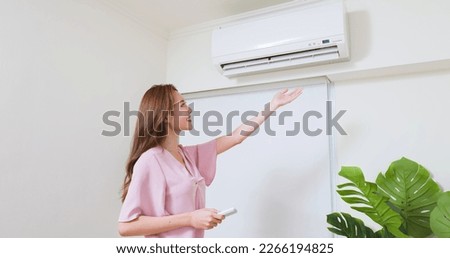 asian woman is turning on air conditioner through switching remote controller at home Royalty-Free Stock Photo #2266194825