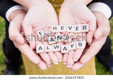Couple holding hand with Forever and Always spelled out on small wooden tiles with a wedding ring as the O in Forever, couple in love