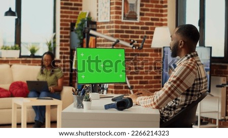 African american man analyzing greenscreen display on computer, looking at isolated template on pc and working remote. Male worker using blank chroma key screen with mockup monitor. Tripod shot.