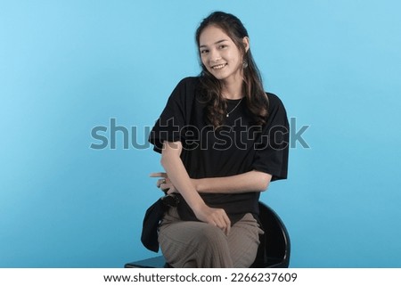 Asian young woman poses to camera wearing black t-shirt on blue background