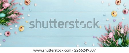 Easter big banner of pink spring flowers, colorful roses, cute bunnies and decorative eggs. Advertising content for Easter holiday on blue wooden background. Flat lay, top view, close up, copy space