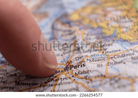 Finger pointing to Paris, France on detailed colorful map with selective focus, shallow depth of field, background blur