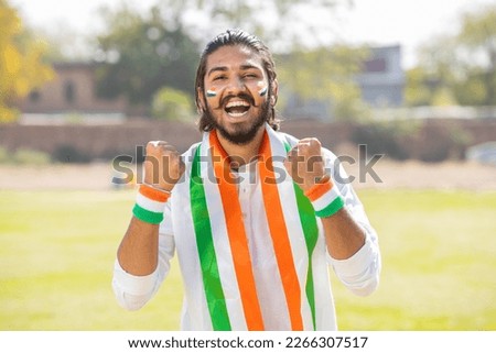 Portrait of cheerful young man fan wearing traditional white kurta and tricolor duppata with face painted cheering for indian cricket, hockey or football team.