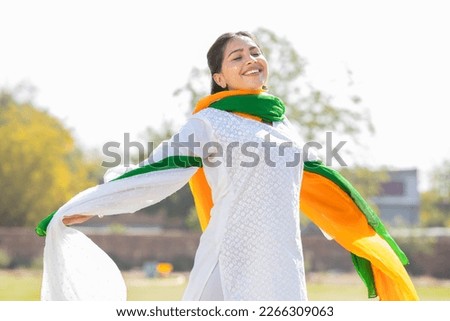 Portrait of happy young indian woman wearing traditional white kurta and tricolor duppata running at park. celebrating Independence day or Republic day. Royalty-Free Stock Photo #2266309063