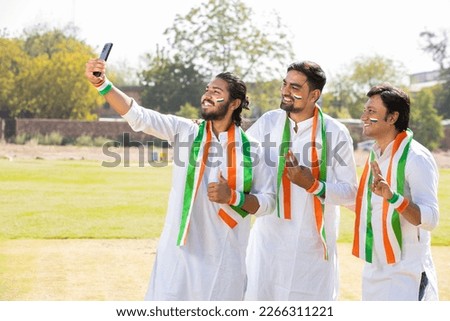 Group Portrait of young indian men wearing traditional white kurta and tricolor duppata taking selife picture with smart phone at park. celebrating Independence day or Republic day. Royalty-Free Stock Photo #2266311221