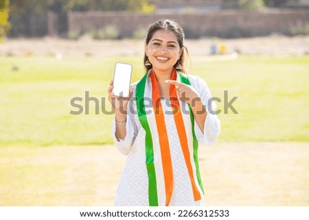 Portrait of young indian woman wearing traditional white kurta and tricolor duppata showing blank display screen smart phone to put advertisement, celebrating Independence day or Republic day. Royalty-Free Stock Photo #2266312533