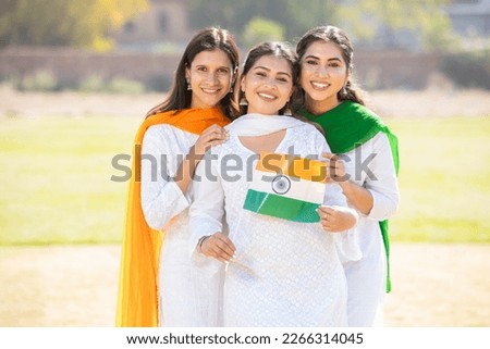 Three young beautiful women wearing traditional white dress holding indian flag while .standing at park together celebrating Independence day or Republic day. Royalty-Free Stock Photo #2266314045