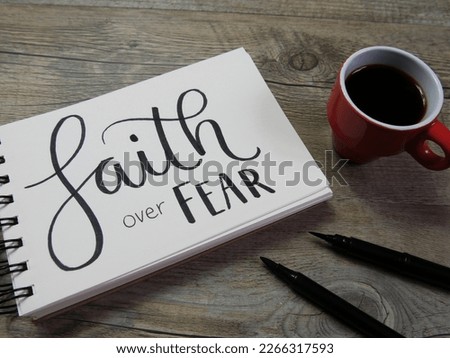 FAITH OVER FEAR lettering in notebook with cup of coffee and pens