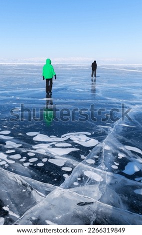Winter holidays on the frozen Baikal Lake. Tourists walk on transparent beautiful blue ice with cracks and bubbles and go skating on sunny February day. Concept of outdoor recreation and activity