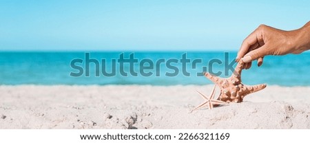 Female hand is touching starfish on a sandy beach. Tropical nature. Banner.