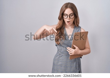 Caucasian woman wearing glasses and business clothes pointing down with fingers showing advertisement, surprised face and open mouth 