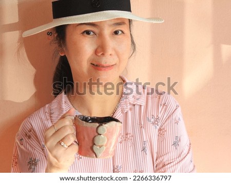 Female with white hat holding coffee mug and looking at camera.