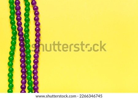 purple and green beads on yellow background Top view 2022 Mardi Gras Parade Schedule Mockup Copy space