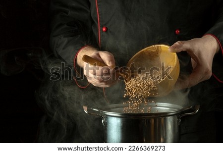 The cook pours dry buckwheat into the pan with a spoon. Dark space for recipe or menu. The idea of cooking delicious buckwheat porridge in the kitchen. Royalty-Free Stock Photo #2266369273
