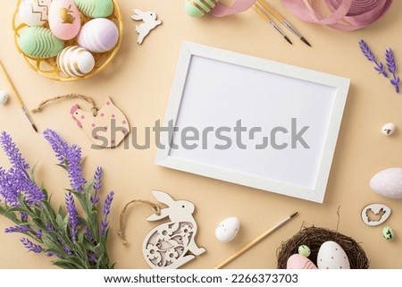 Easter concept. Top view photo of photo frame paintbrushes colorful easter eggs in bowl wooden bunnies chicken pink ribbon nest and lavender flowers on isolated beige background with copyspace