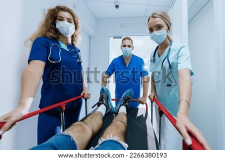 First-person view.Three doctors are rolling a gurney with a patient in the hospital corridor. Emergency hospitalisation in the clinic. Selective focus on the male doctor. Royalty-Free Stock Photo #2266380193