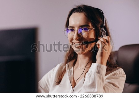 Hotline operator in headset looking at the computer screen. Smiling support agent girl at her workplace. Portrait of happy female call center worker