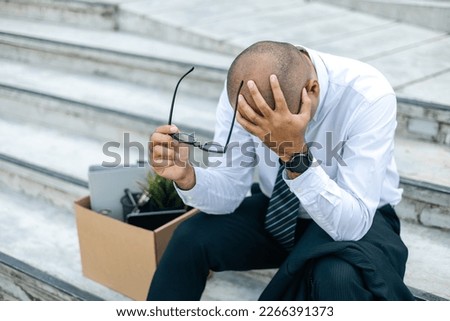 Sadness depressed Businessman with box cardboard packing personal items after losing jobs. Failure businessman sitting at stair front of building. Your fired Unemployed Jobless People Crisis Royalty-Free Stock Photo #2266391373