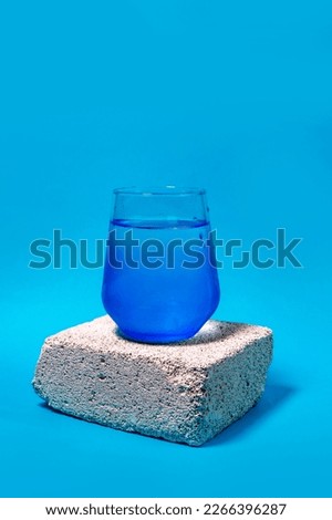 blue transparent glass with clear water and water drops on white brick isolated on turquoise blue background, vertical, copy space 